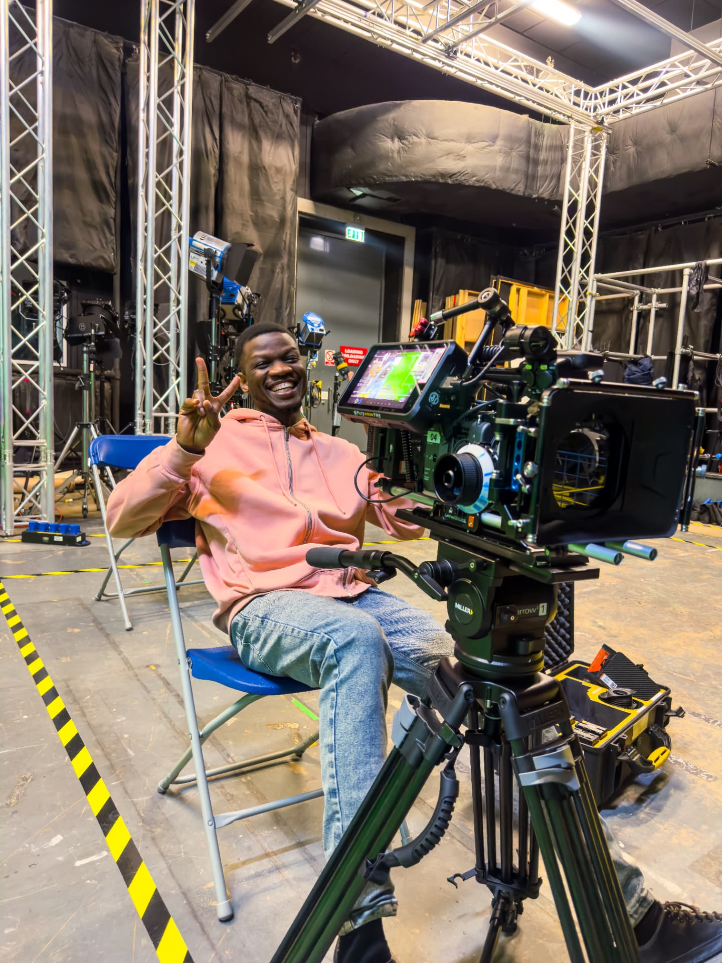 Favour Amuele seated beside a cinema camera on a studio set